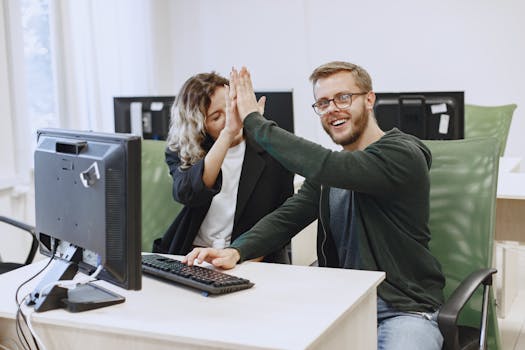 两名同事在现代办公室的电脑屏幕前击掌，象征着团队合作