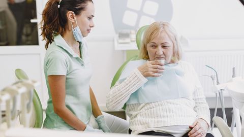 A female dentist assists a senior patient in a dental clinic, ensuring comfort and care.