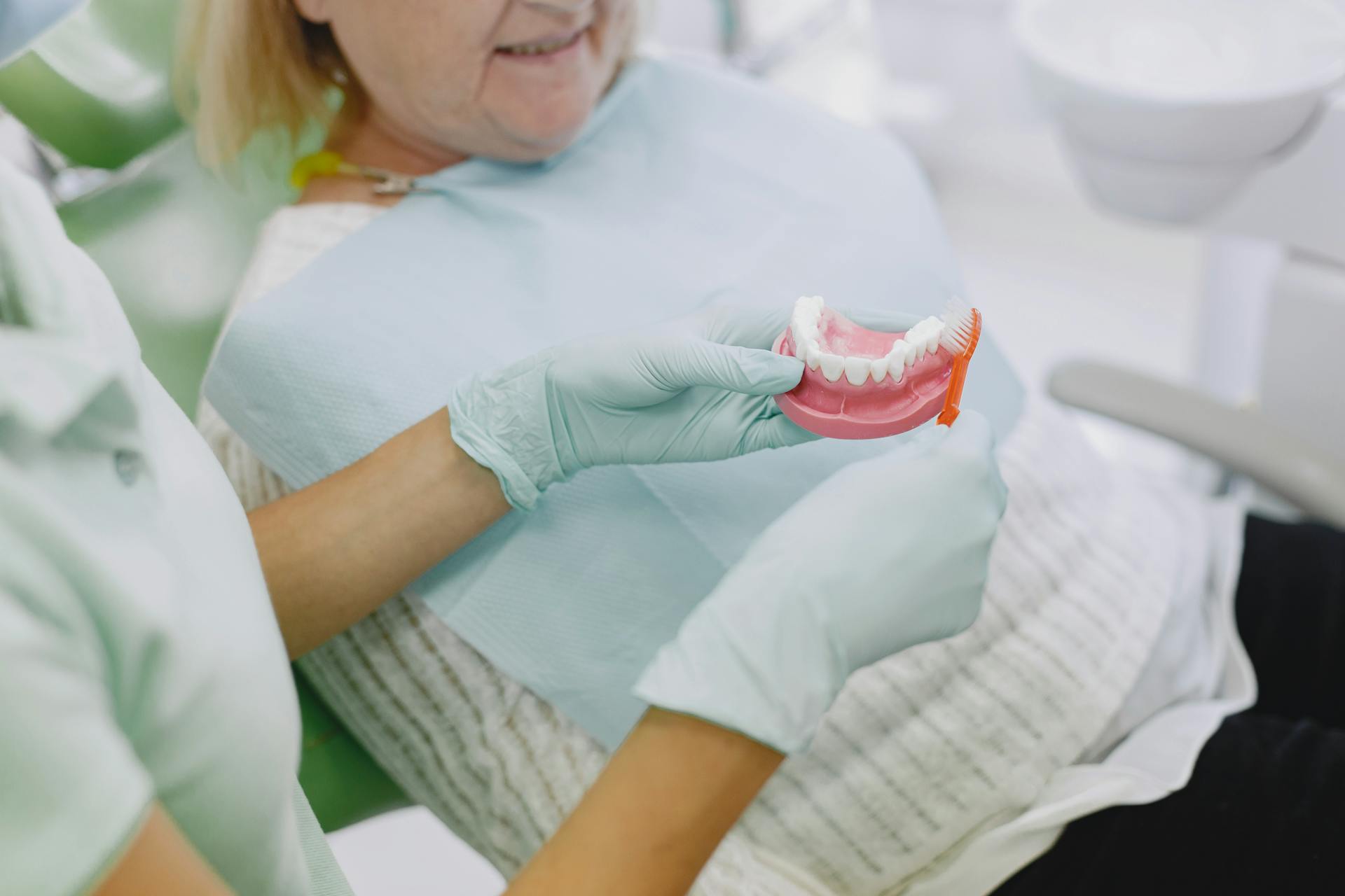 Senior woman in dental chair being shown denture brushing technique by a dental professional.