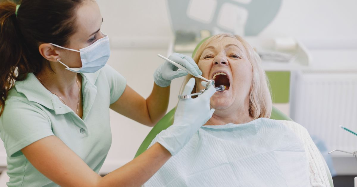A dentist wearing a mask and gloves examining a senior woman's teeth and gums in a dental clinic