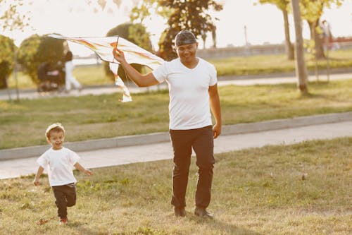 A Man Walking at the Park with His Son while Holding a Kite