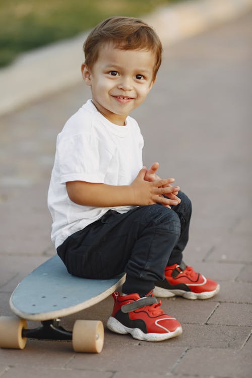 A Young Boy Smiling while Sitting on a Skateboard