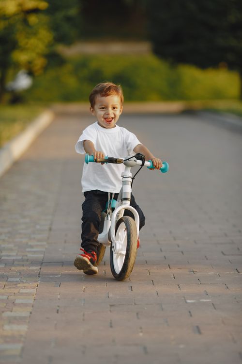 Free A happy child rides a bicycle outdoors on a sunny day, smiling broadly. Stock Photo