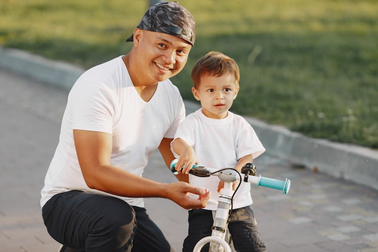 A Man Smiling With His Son Beside Him Riding A Bike