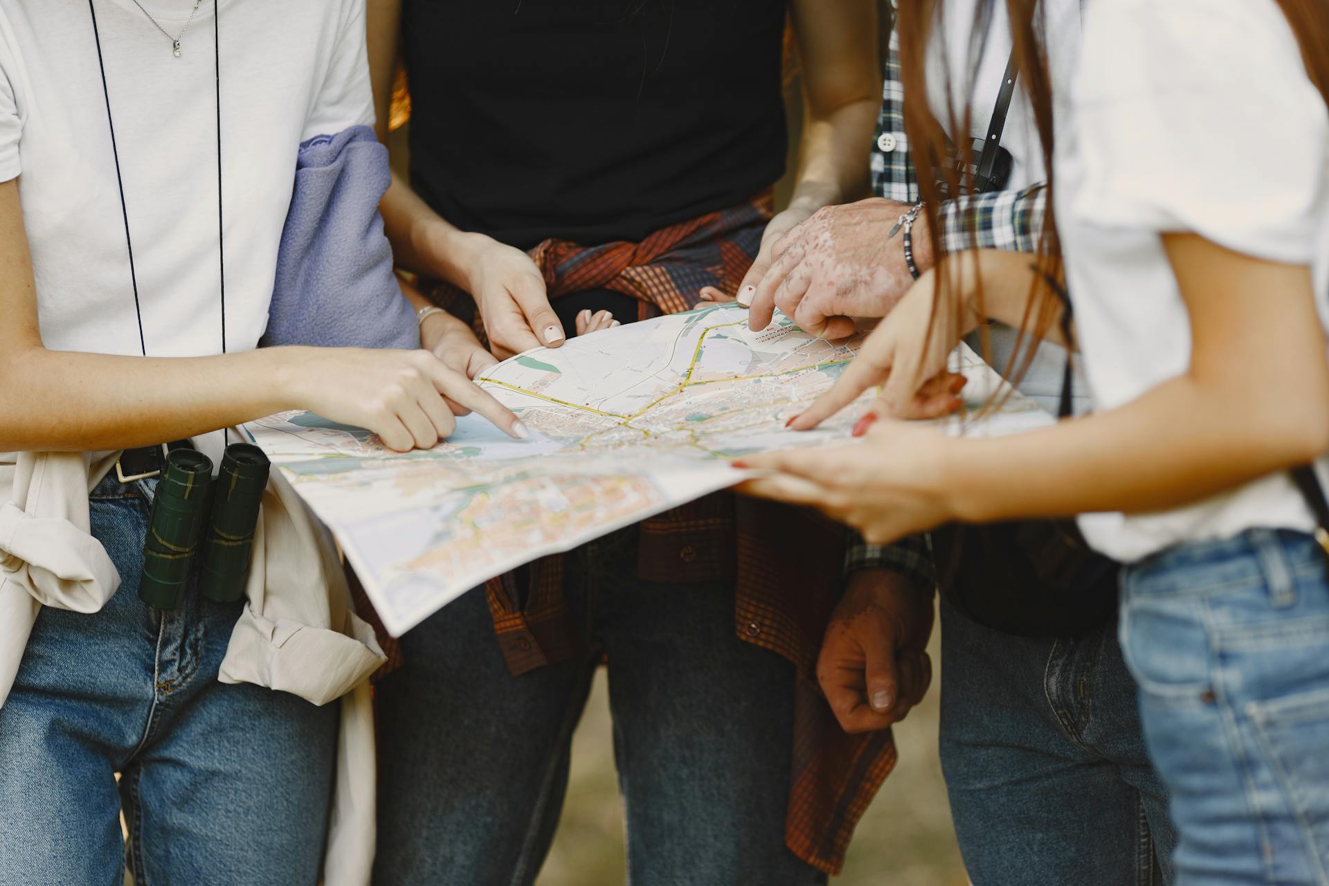 Young adults examining map on outdoor exploration, daytime travel planning.