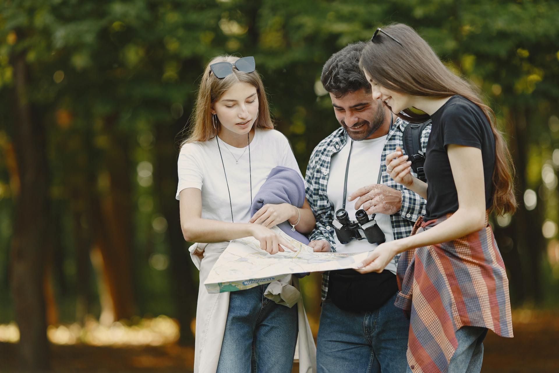 Three friends study a map in a sunny park, planning their adventure with smiles and excitement.