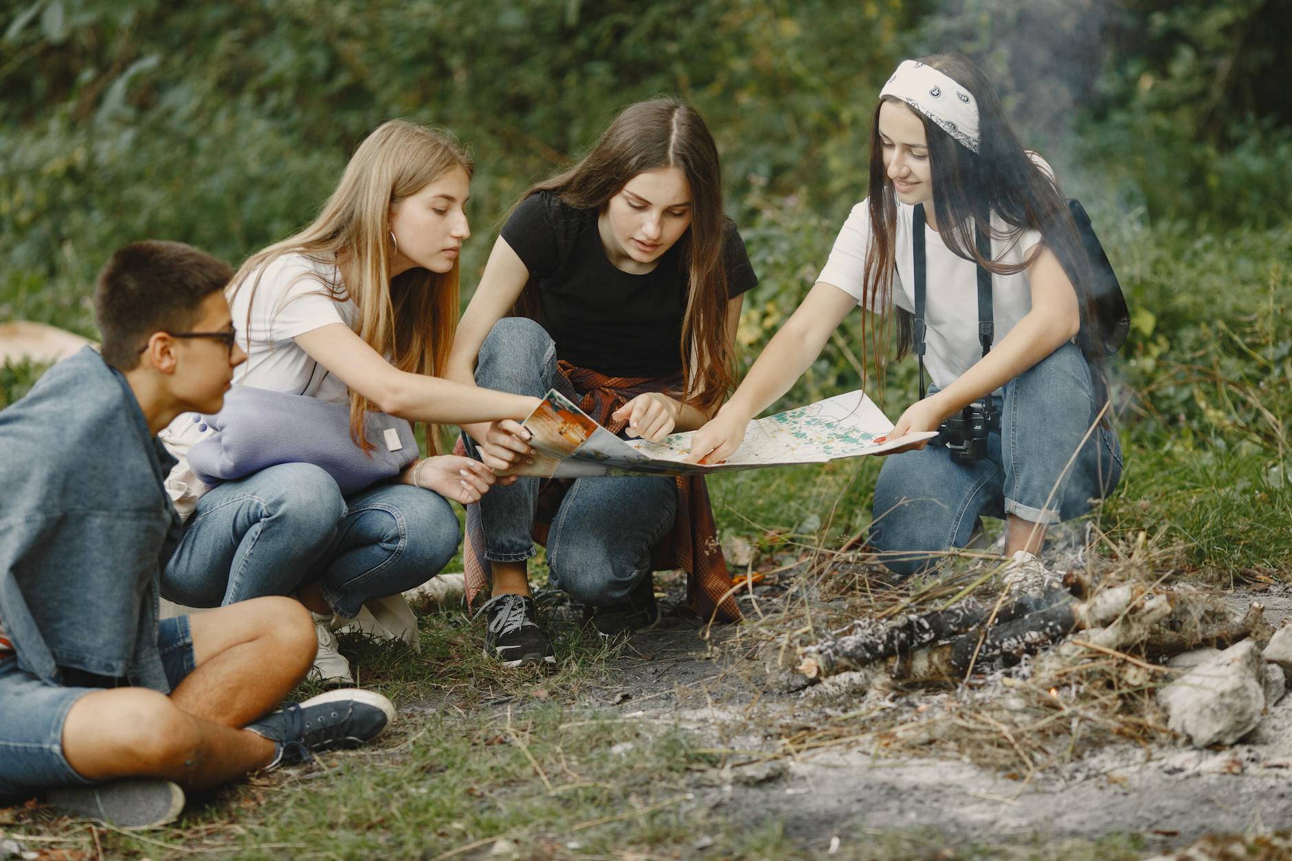 Group of teens sitting around a campfire, planning adventure with a map.
