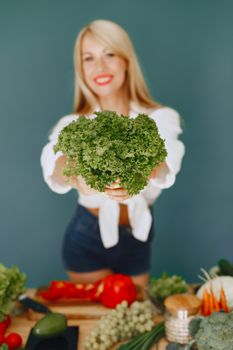 Smiling woman holding fresh kale surrounded by vibrant vegetables. Healthy lifestyle concept.