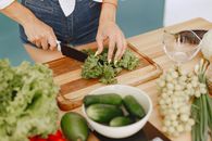 Person Slicing Green Vegetable on Brown Wooden Chopping Board
