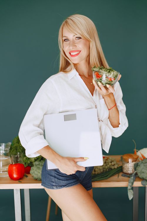 Free Cheerful woman holding a salad and scale, promoting a healthy lifestyle with fresh vegetables. Stock Photo