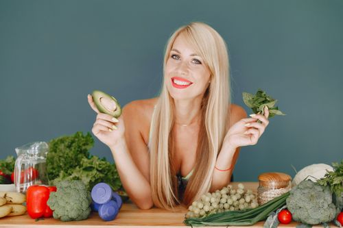 Free Blonde woman promotes healthy eating with fresh vegetables and fruits on display. Stock Photo