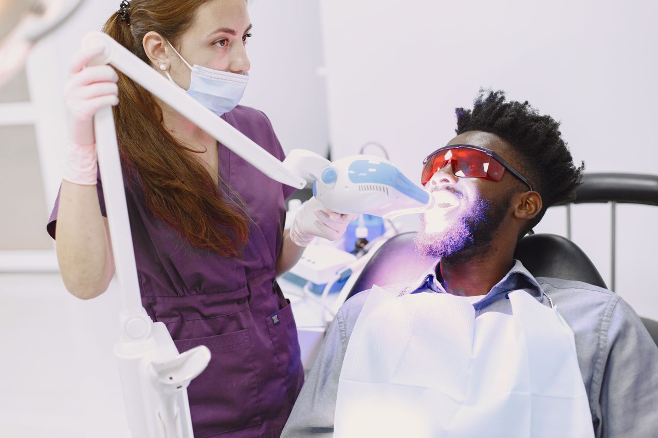 Dentist performing teeth whitening procedure with specialized equipment