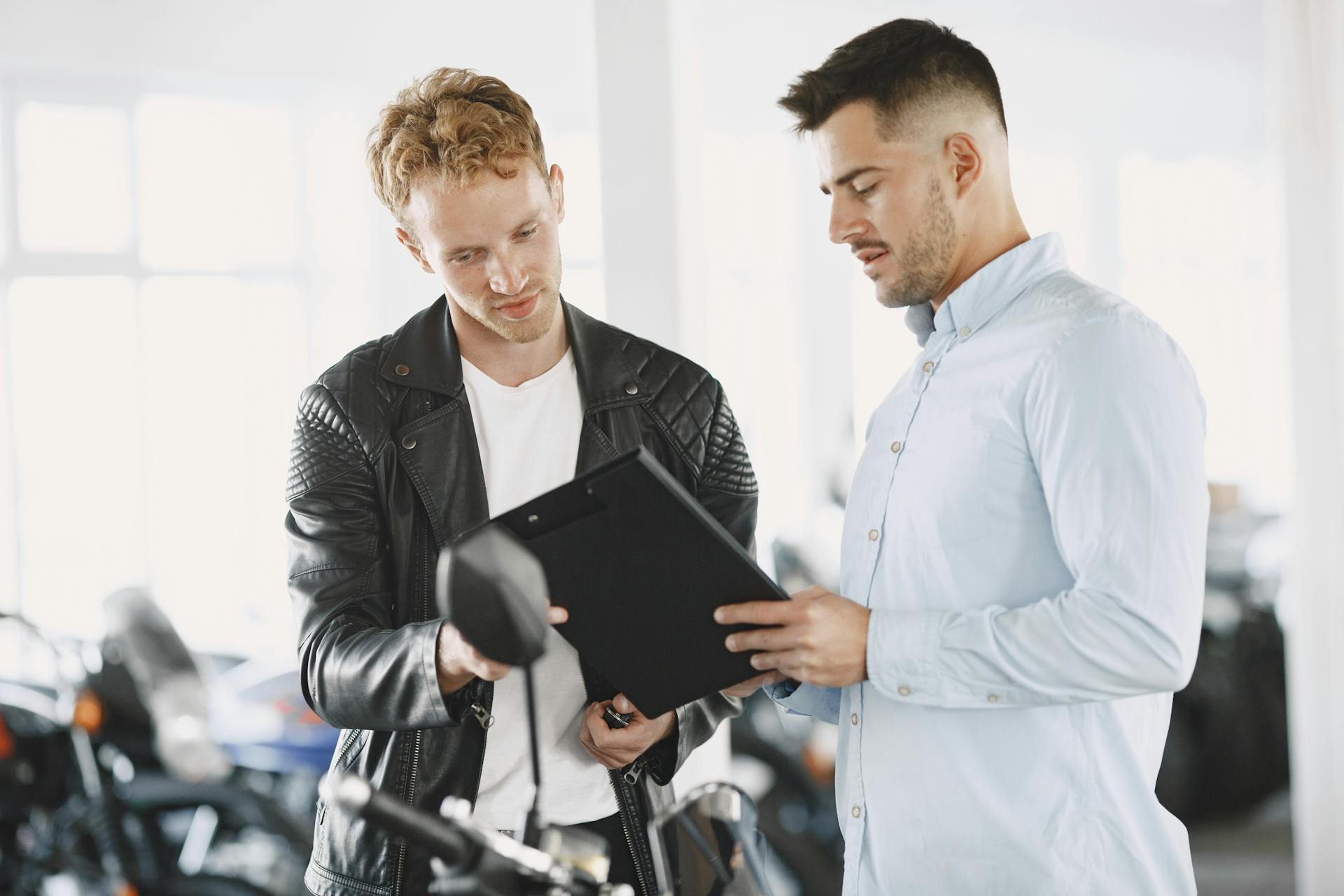 Two men reviewing documents in a motorcycle dealership, discussing a purchase agreement.