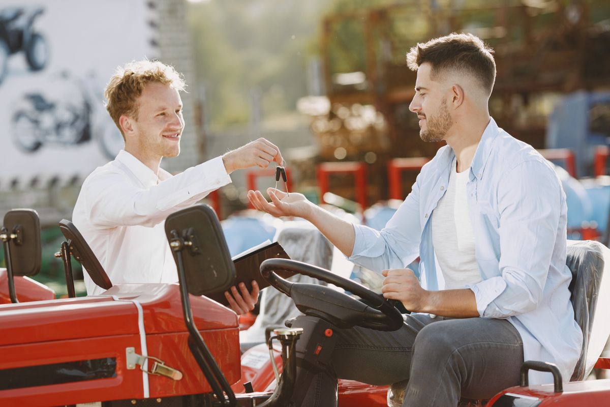 A seller handing tractor keys to a buyer at an outdoor equipment lot