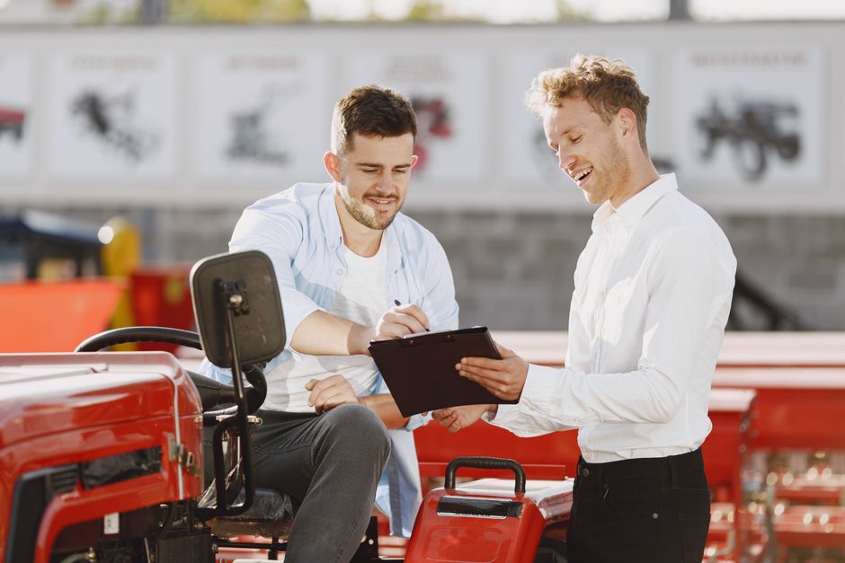 Two men discussing tractor purchase, collaborating outdoors with clipboard. Two men discussing tractor purchase, collaborating outdoors with clipboard.