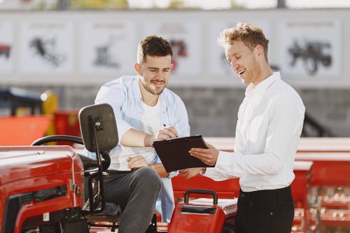 Free Two men discussing tractor purchase, collaborating outdoors with clipboard. Stock Photo