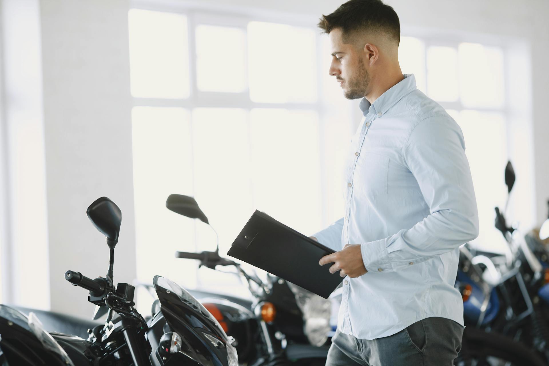 Man examining motorcycles with a clipboard in a dealership showroom.