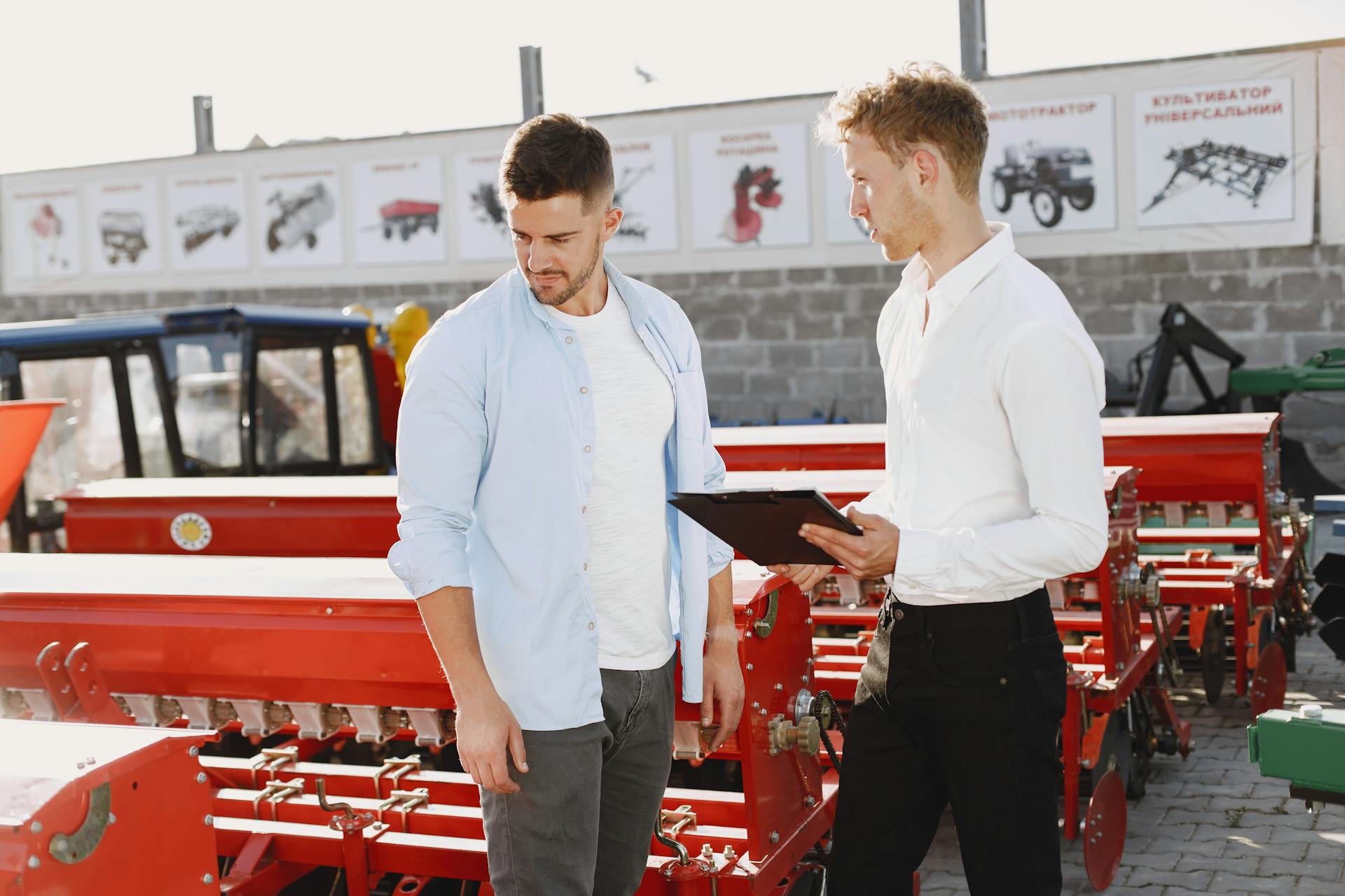 Two men discussing agricultural equipment at an outdoor store during the day.