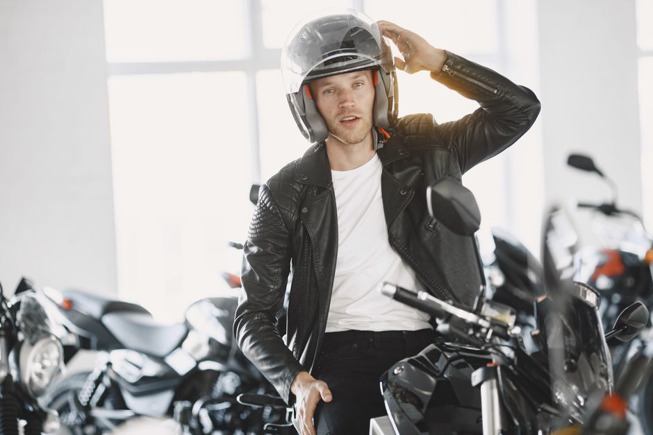 Man in leather jacket with helmet on a motorcycle indoors, ideal for lifestyle and automotive themes.