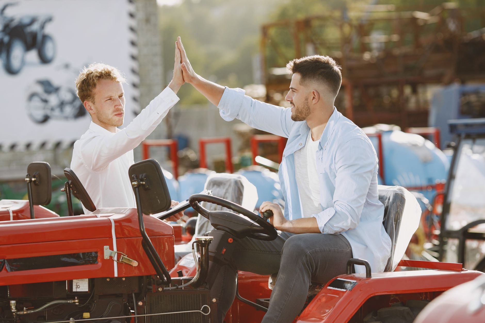 Two men enthusiastically high-five after a successful tractor purchase in an outdoor setting.