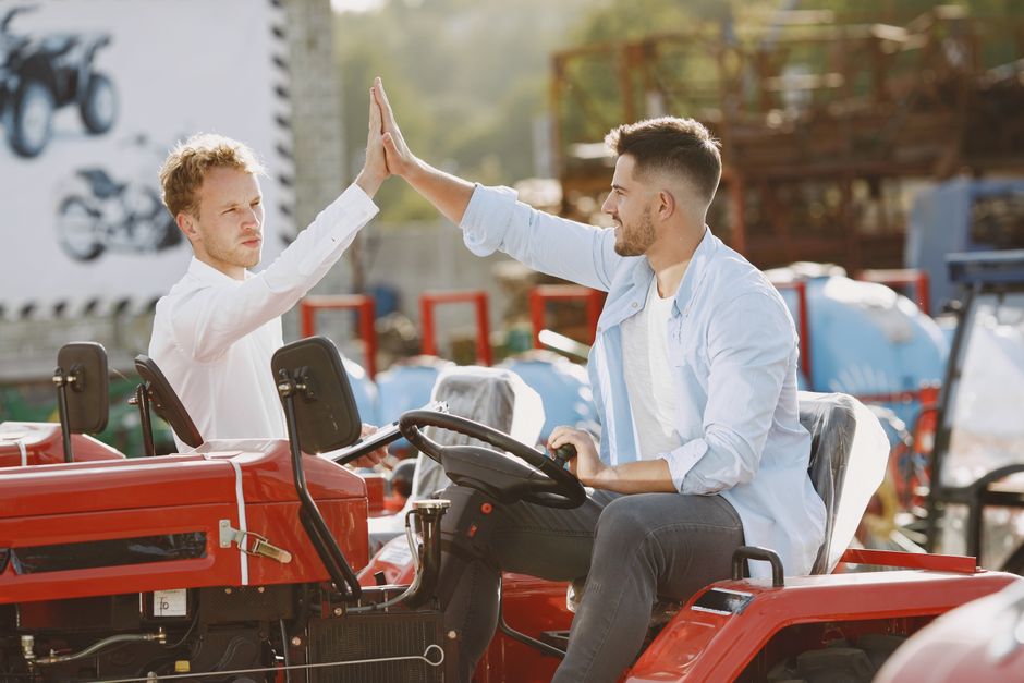 Two men enthusiastically high-five after a successful tractor purchase in an outdoor setting. Two men enthusiastically high-five after a successful tractor purchase in an outdoor setting.