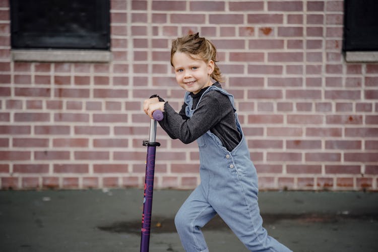 Cheerful Kid On Scooter Near Urban Building