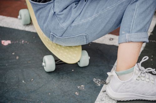 Free Crop anonymous child in jeans and sneakers sitting on penny board while having break from riding Stock Photo