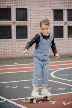 Full length of adorable child in casual outfit riding skateboard while practicing on sports ground