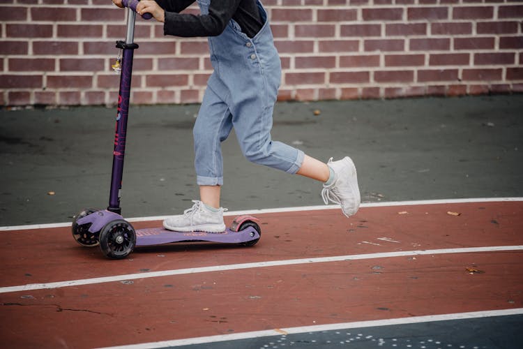 Crop Kid Riding Scooter On Sports Ground