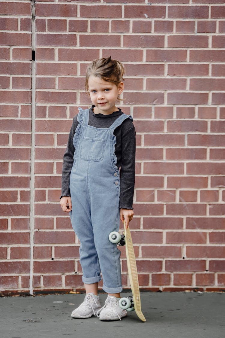 Little Girl With Skateboard Near Brick Wall