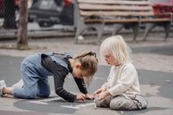 Focused little girls drawing on asphalt