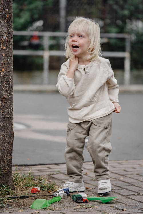Free Full body adorable excited little girl in casual outfit standing near tree with toys and calling friend looking away Stock Photo
