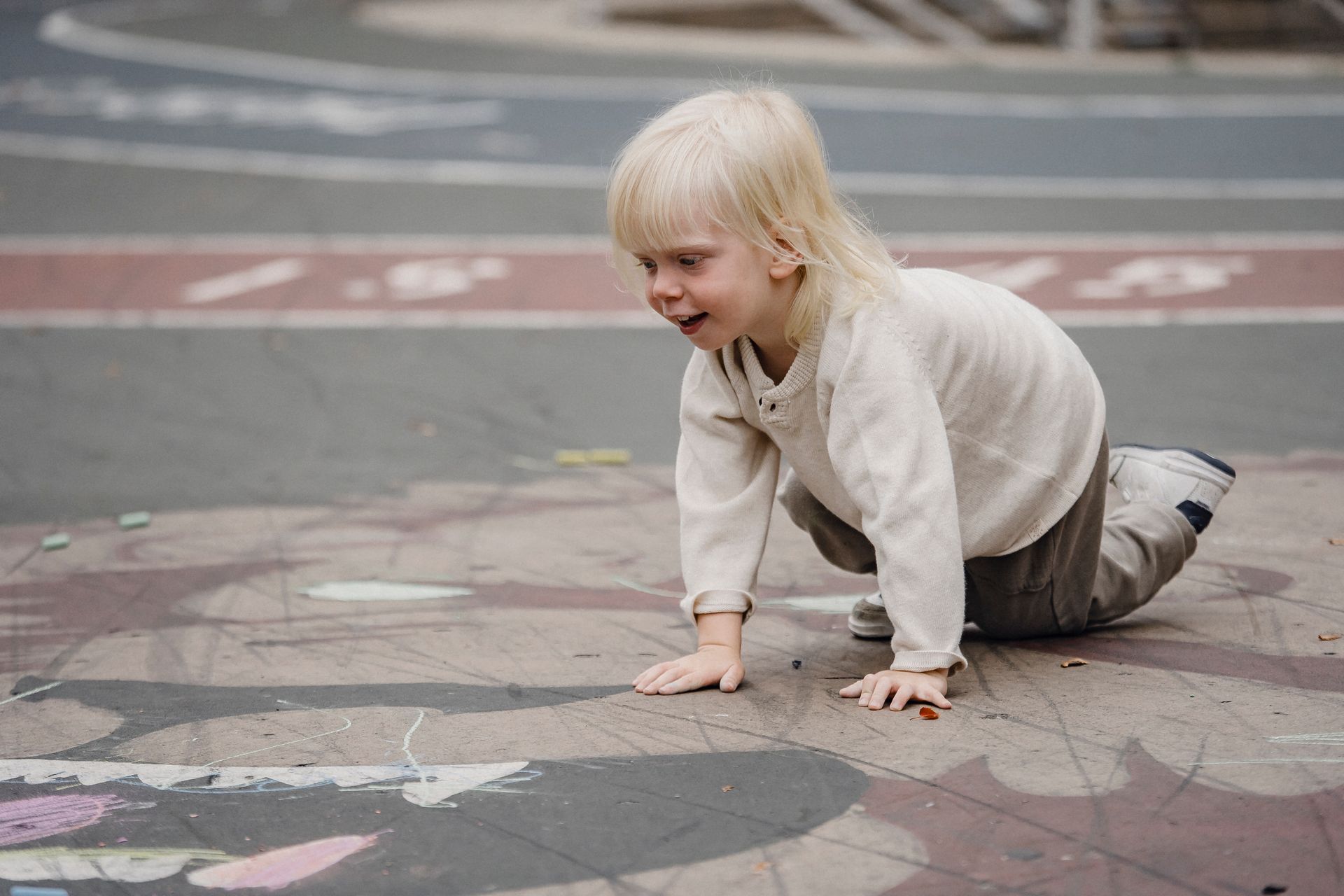 A toddler crawling outdoors on pavement covered in chalk drawings