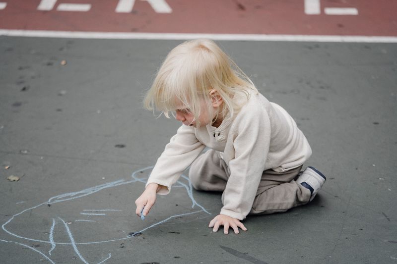 Little kid drawing with chalk on asphalt, focused and concentrated