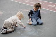 两个年幼的孩子正专注地在户外人行道上用粉笔画画，发挥他们的创造力