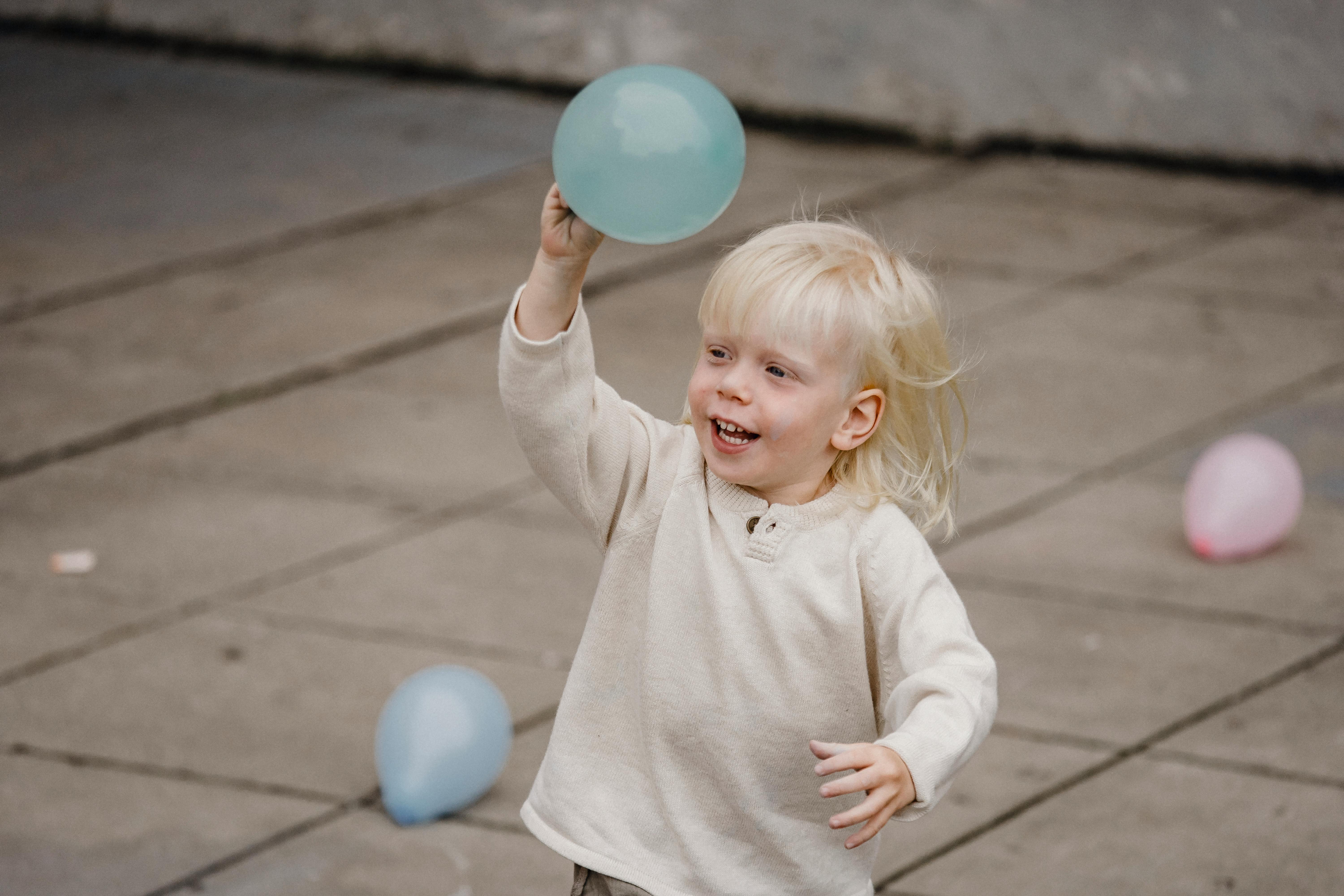 happy little boy raising hand with balloon on street