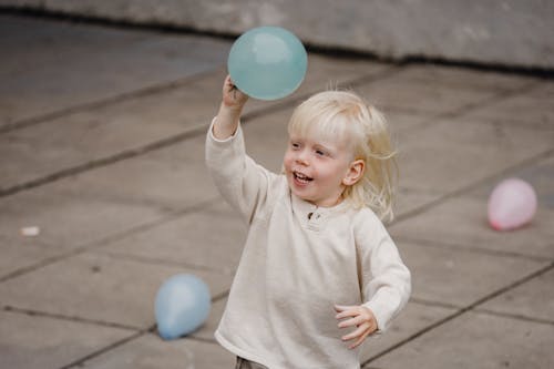 Happy little boy raising hand with balloon on street