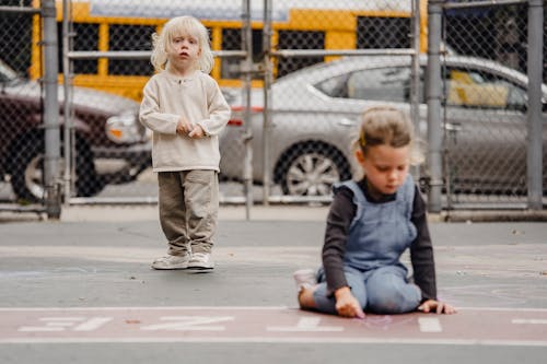 Free Full body positive little kids in casual clothes drawing with chalks on asphalt ground in daylight Stock Photo
