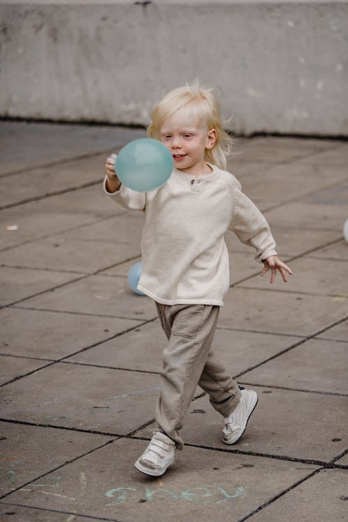 Adorable boy with balloon walking on pavement