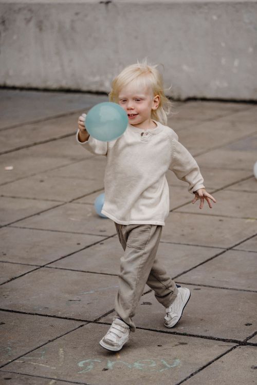 Free Full body content little boy in casual outfit playing with green balloon and walking on paved sidewalk Stock Photo