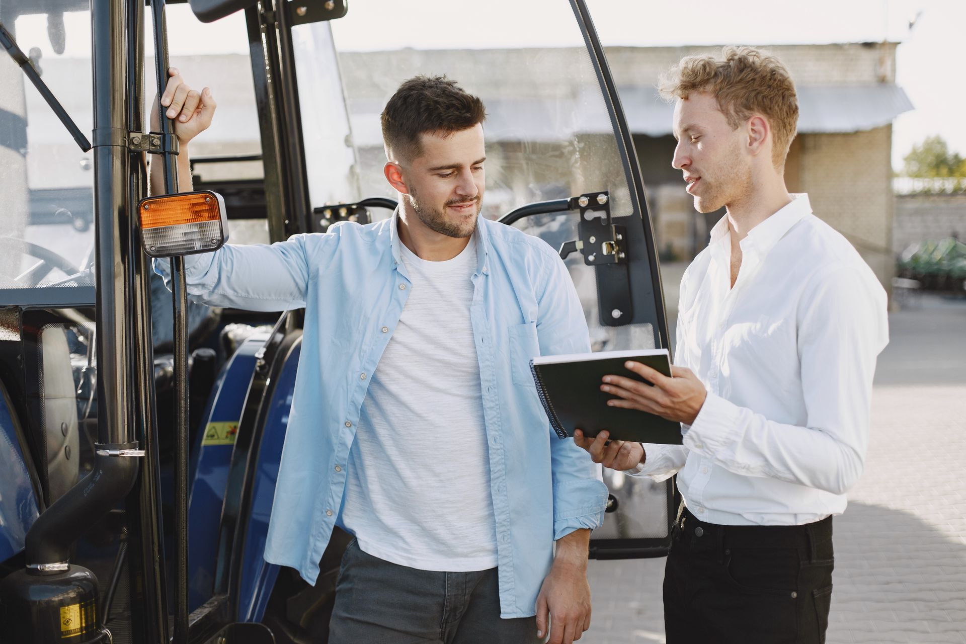 Two men discussing business plans beside a blue tractor outdoors.
