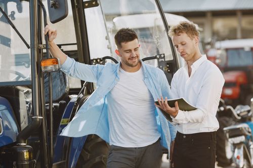 Free Two businessmen discussing a vehicle purchase outdoors with a tractor in the background. Stock Photo