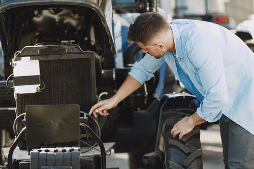 Free A mechanic in a blue shirt inspects a car engine outdoors, ensuring proper function. Stock Photo