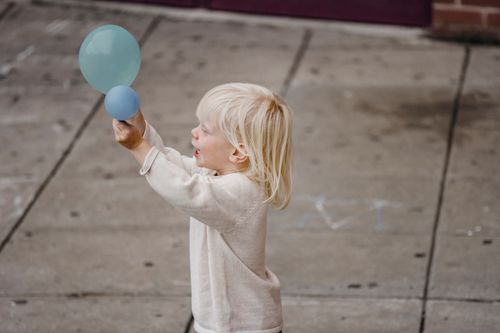 Free Side view joyful little boy in casual white clothes playing with balloon on paved sidewalk Stock Photo