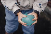 From above of crop anonymous kid in casual clothes with ornament pressing blue balloon in daylight