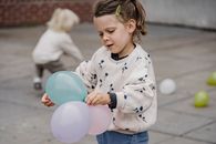 Crop charming child in ornamental apparel standing with assorted balloons on street with anonymous best friend playing in daytime
