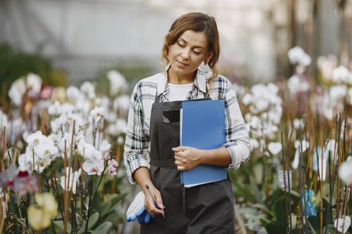 Free Woman gardener in greenhouse holding a notebook, surrounded by blooming orchids. Stock Photo