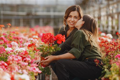 Free A mother and daughter share a joyful moment surrounded by vibrant flowers in a garden. Stock Photo