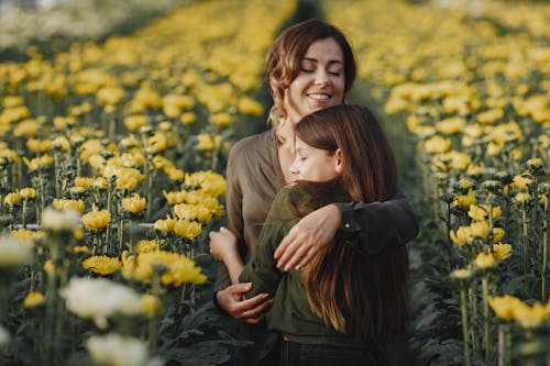 Mom Hugging Her Daughter Near Blooming Yellow Flowers