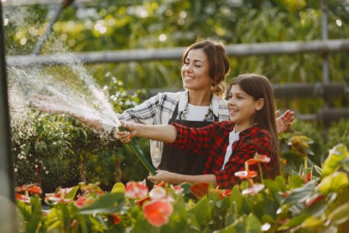 Free A mother and daughter joyfully watering plants in a vibrant garden setting. Stock Photo